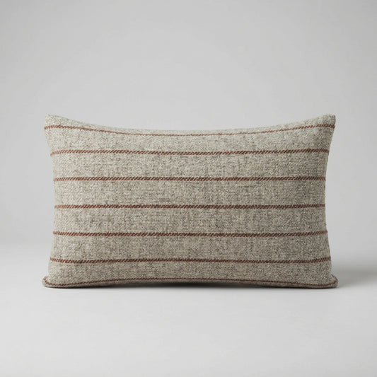 A rectangular cushion in a woven beige fabric with thin horizontal rust stripes, resting on a surface against a plain white wall.