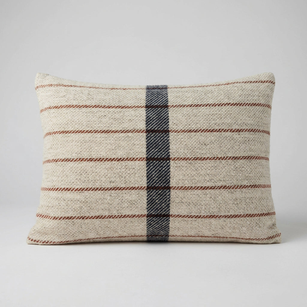 Rectangular oatmeal wool cushion with thin rust horizontal stripes and a wide navy stripe down the centre, against a plain grey background