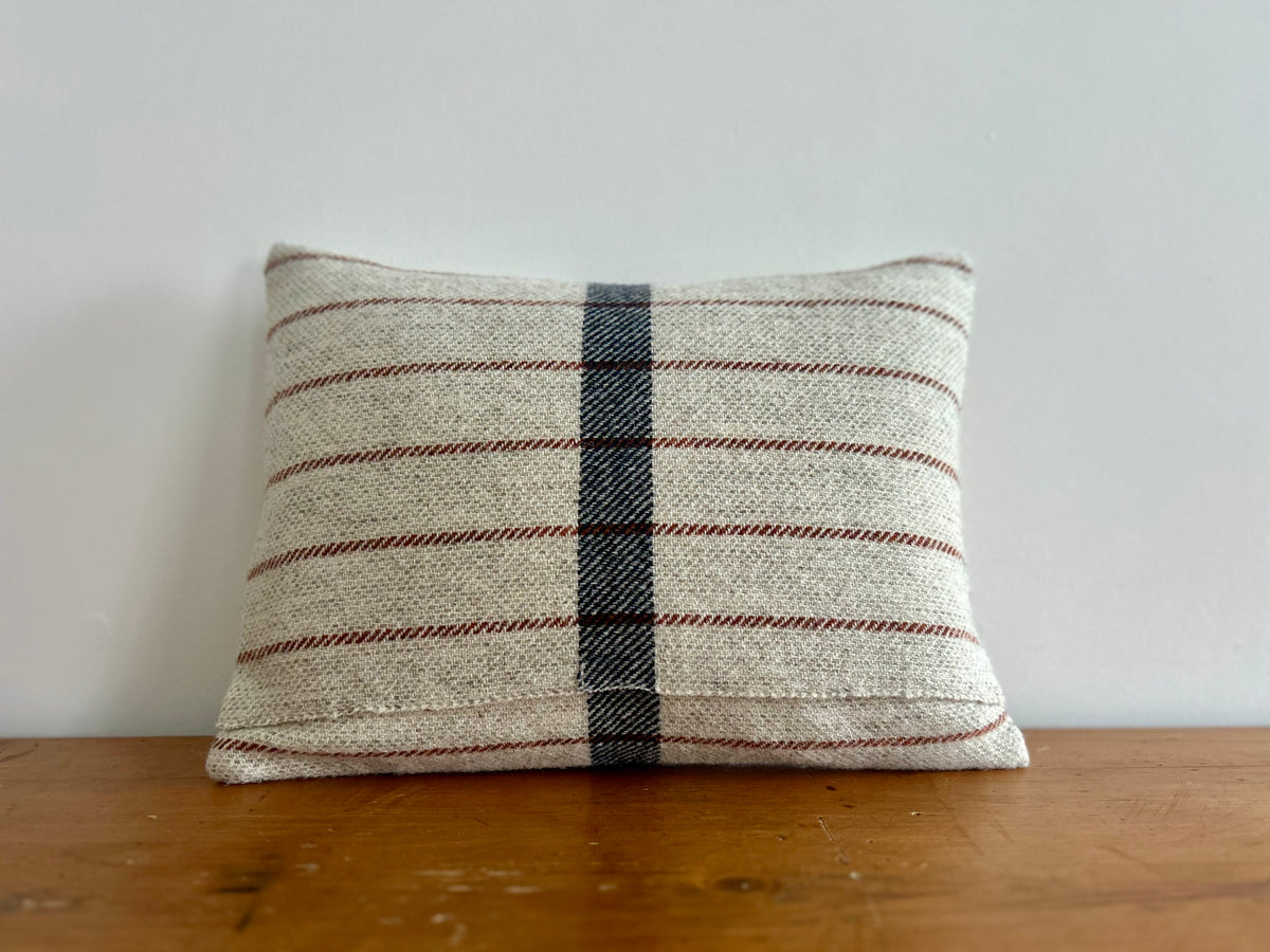 Back of the oatmeal wool cushion with rust stripes and a navy centre stripe, showing the envelope-style opening