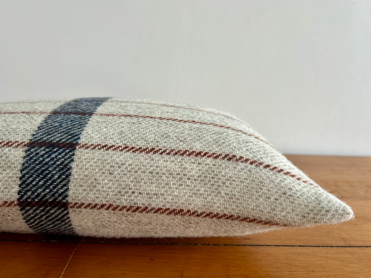 Side view of the oatmeal wool cushion with rust and navy stripes, lying on a wooden surface to show its thickness
