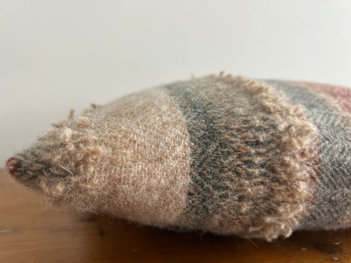 Corner of the cushion up close, showing the soft, fuzzy wool and looped yarn band in oatmeal and grey-green