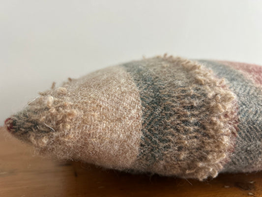 Corner of the cushion up close, showing the soft, fuzzy wool and looped yarn band in oatmeal and grey-green