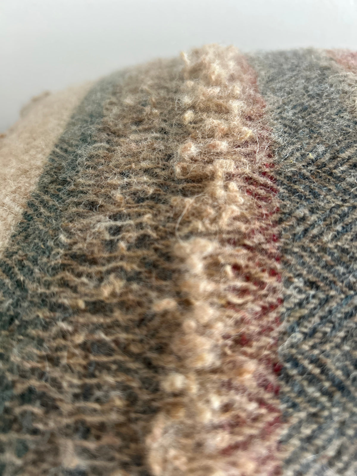 Close-up of the textured fringed band in tan and grey-green wool, next to a brick red and navy herringbone stripe
