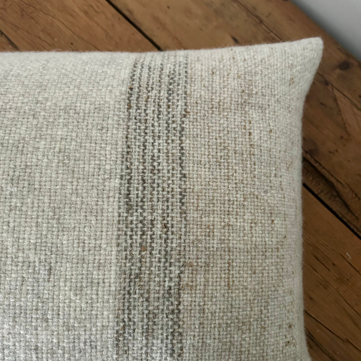 Close-up of the woven oatmeal wool with fine grey stripes and flecks of tan, resting on a wooden surface